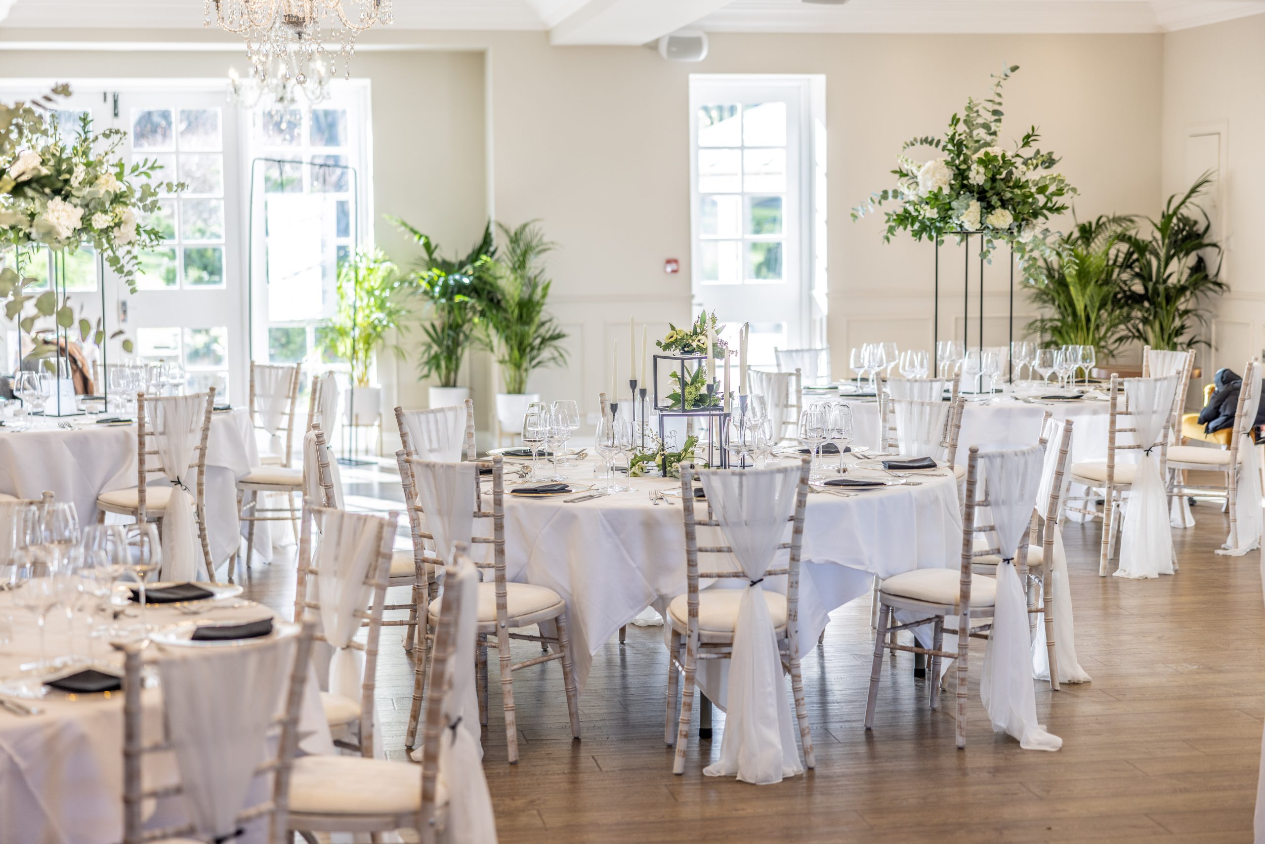 A reverse angle of the fully-decorated Lowry room for a wedding reception, with chairs around round tables featuring table decorations