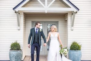 Bride and groom standing outside the Coast House, holding hands and looking at each other