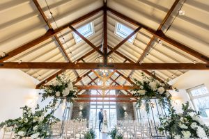 The trusses of the Coast House, with the bride and groom at the front of the wedding ceremony in the fully-decorated Coast House, with multiple rows of chairs