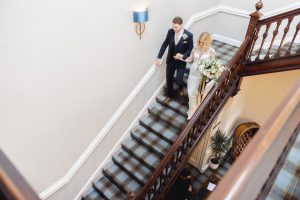 Bride and groom walking down the stairs inside the manor house, hand-in-hand